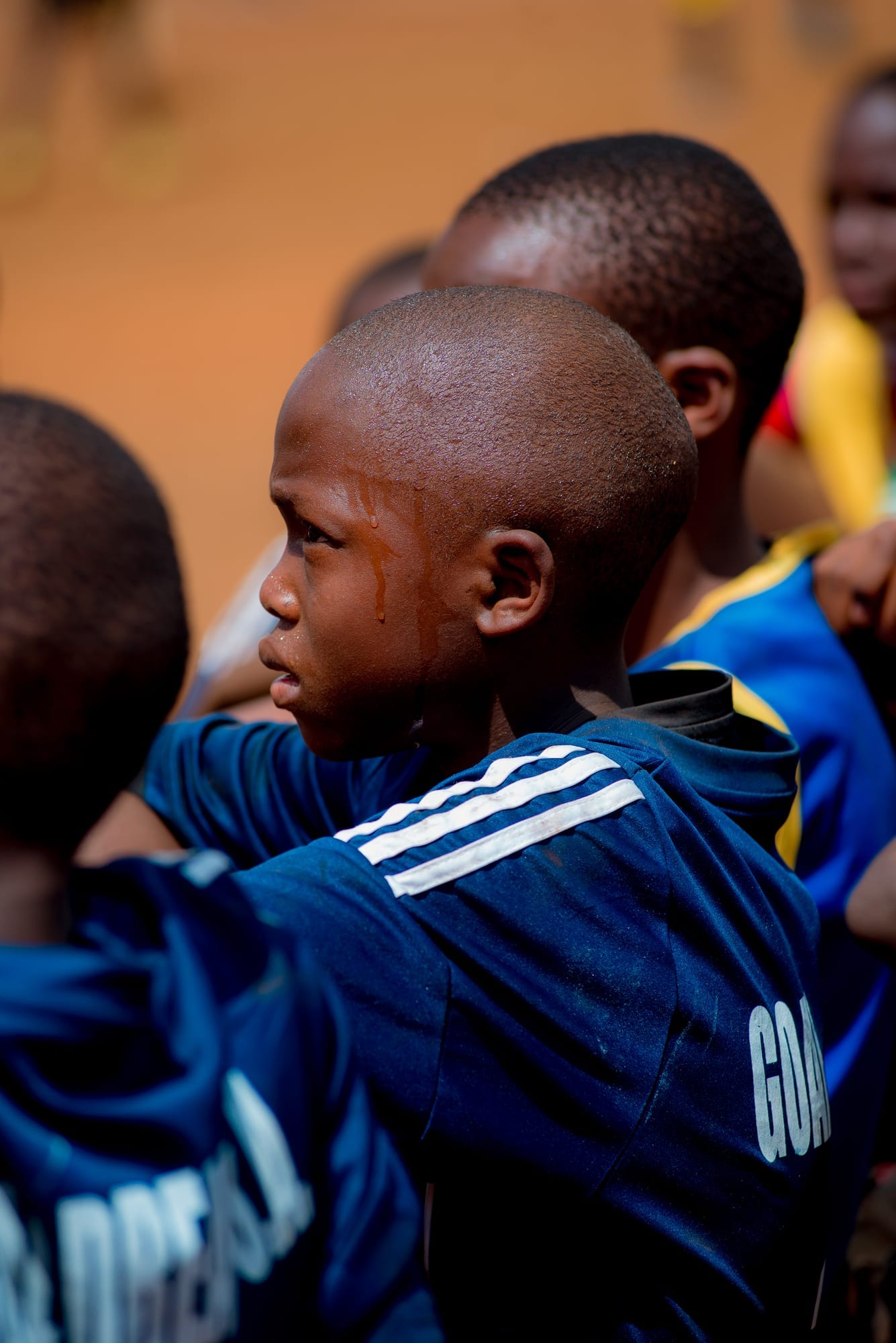 A Goal Dream player in a navy training top, sweat running down his face, stands in profile with his arm across a team-mate's shoulders alongside the rest of the group